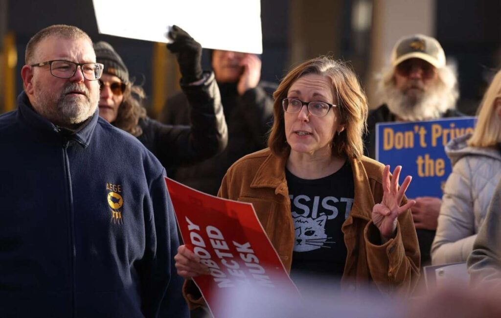 Pat Kearns, left, president of AFGE Local 2547, watches March 6, as Jennifer Sherer addresses protesters who gathered in front of the Davenport office of Republican U.S. Rep. Mariannette Miller-Meeks. (Roy Dabner/Quad-City Times)