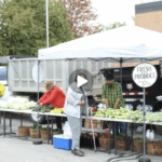 A woman stands at a farmers market stand