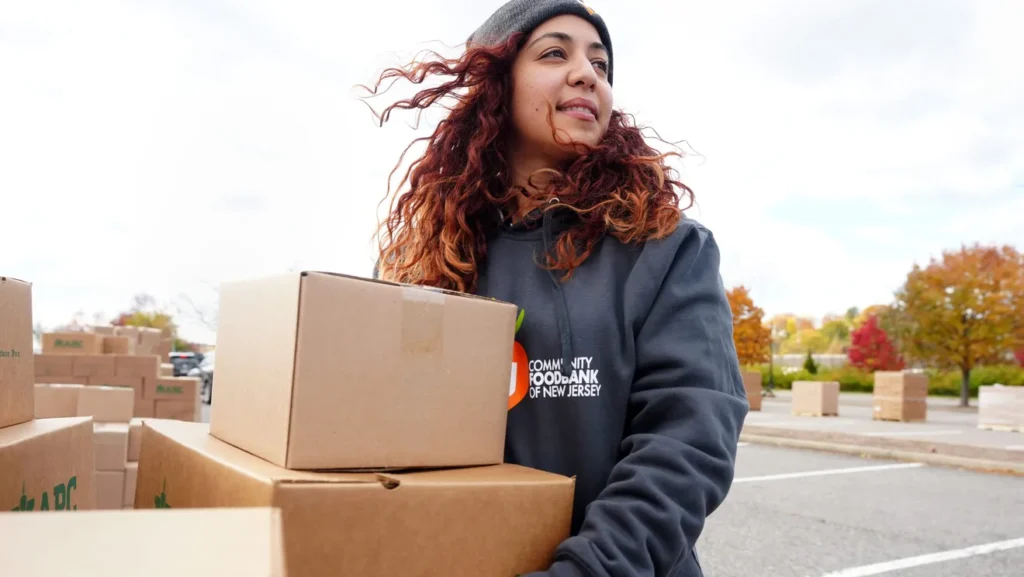 A woman carries boxes full of food towards her local foodbank. 