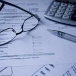 Glasses, a pen and a calculator strewn across bills