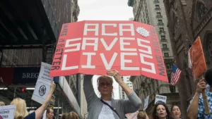 A woman holding a protest sign that says "ACA Saves Lives" - Albin Lohr-Jones/Pacific Press/Zuma