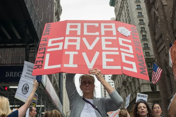 A woman holding a protest sign that says "ACA Saves Lives" - Albin Lohr-Jones/Pacific Press/Zuma
